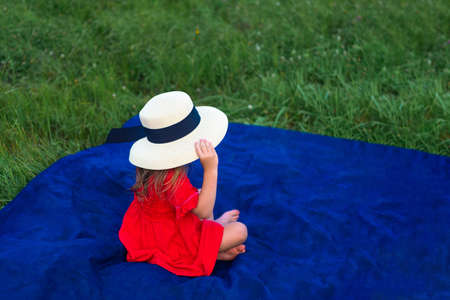 girl in a hat and in a red dress sunbathes on the green grass. No faceの写真素材