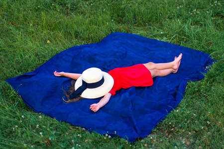 girl in a hat and in a red dress sunbathes on the green grass. No face
