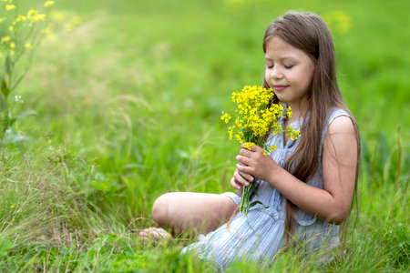 A girl with long hair in a field sniffing yellow flowersの写真素材