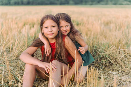 two happy sisters are sitting in a field in the hay and huggingの写真素材