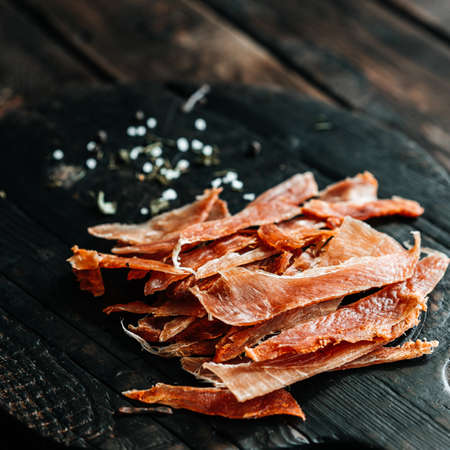 Dried chicken cut into strips on a wooden board with salt and pepperの写真素材