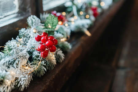 Christmas garland with red berries and snow on the tree, on the window.の写真素材