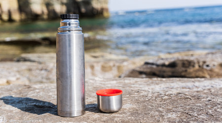 Thermo flask and mug on stone on the beach at sunset near the sea. high quality photoの写真素材