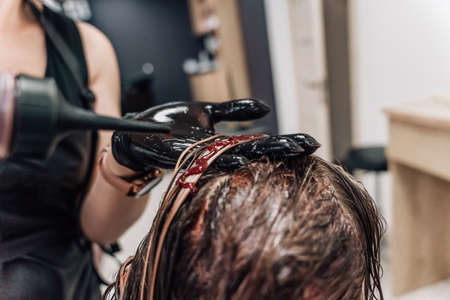 Female hands of a hair master. Close-up of blond hair on a curling iron. Curling curls. high quality photoの写真素材