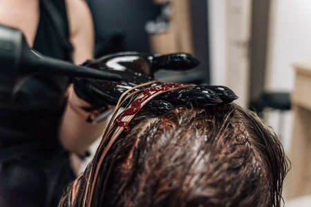 Female hands of a hair master. Close-up of blond hair on a curling iron. Curling curls. high quality photoの写真素材