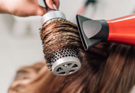 Drying long brown hair with a blow dryer and a round brush. close. high quality photoの写真素材