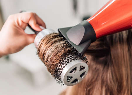 The hairdresser dries long brown hair with a round brush. high quality photoの写真素材