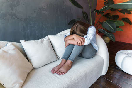 Portrait of a beautiful young woman with a depressed expression sitting on a sofa. Sad woman in her...