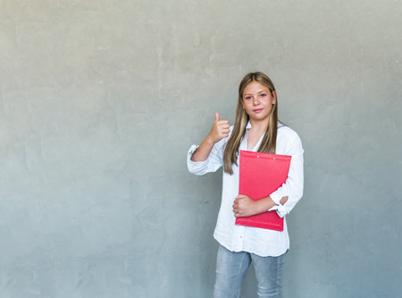 A young woman attends courses, a female student studies, holds notebooks and shows a thumbs up in approval, recommending. high quality photoの写真素材