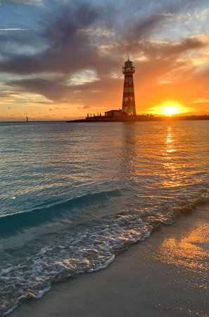 Beach in the foreground and the sun falling on the horizon with a lighthouse in the background.Summer holiday conceptの写真素材