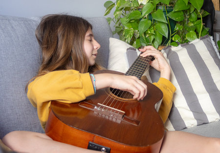 Young girl enjoying her guitar on a sunny morning at home. Playing instruments concept. Horizontal...
