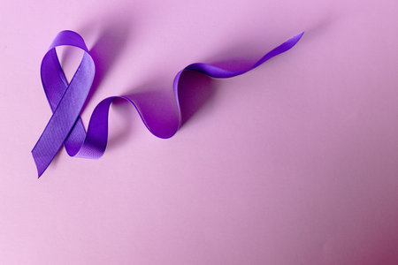 Purple ribbon on pink background symbolising Cancer consciousness.の写真素材