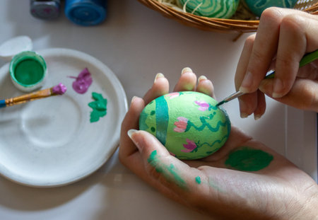 Close up of hand holding brush and paints egg for Easter holidays.Easter Decoration Tradition...
