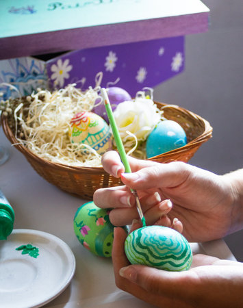 Hand holds brush and paints egg for Easter vacation.Easter Decoration Tradition Concept. Spring season.Homemade painted Christian decorationの写真素材