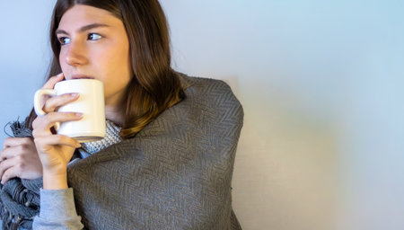 Close-up of a woman drinking tea and looking aside .Neutral background. Space for text