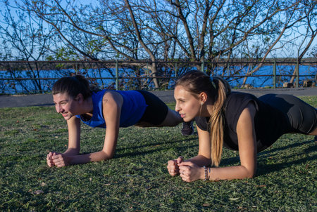 Two young women enjoying outdoor fitness in park, healthy and active living. Beautiful river...