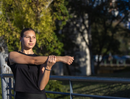 Beautiful teenage girl stretching in park at sunset, outdoor fitness and wellness lifestyle. Horizontal real picture with space for text. Especially for sports campaigns, healthy outdoor living. Concept of young people playing sportsの写真素材
