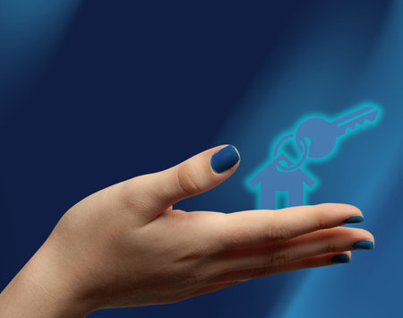 Female hand with key symbol representing home ownership. Blue background.. Perfect for mortgage ads, realtor visuals, and housing promotions.の写真素材
