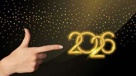 Female hand pointing golden 2026 numbers with sparkling lights, perfect for New Year banners,...