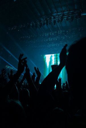 Vertical shot of a rock concert with silhouettes of fans enjoying the musical performance. Fans...