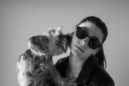 Blonde woman wearing sunglasses and a black leather jacket posing with her little dog Black and white portrait, perfect for advertising, fashion lookbooks, and brand storytelling.の写真素材