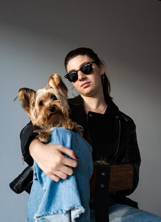 Blonde woman in casual streetwear posing with ser little yoorkie against minimalist gray wall. Perfect for editorial use, street photography, and style magazines.の写真素材