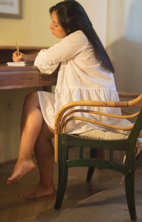 Young woman writing thoughts on notebook at desk. Romantic portraitの写真素材