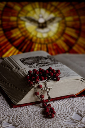 Religious still life showing essential Christian symbols with a lit candle. White rose. Red rosary...