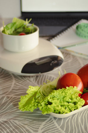 Kitchen scale featuring fresh garden vegetables like lettuce and tomatoes, representing a conscious effort towards mindful eating, calorie counting, and promoting a balanced diet for overall healthの写真素材