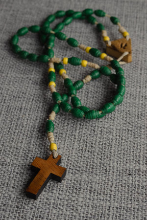 Rosary of green and yellow beads with a simple wooden cross on a grey background symbolizing faith,...