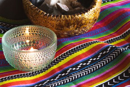Burning candle in a glass holder and a bowl filled with light colored stones resting on a brightly...
