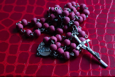 Rosary with red wooden beads and crucifix laying on a red textured surface, symbolizing faith,...