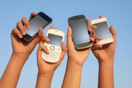 hands holding phones with blue sky as backgroundの写真素材