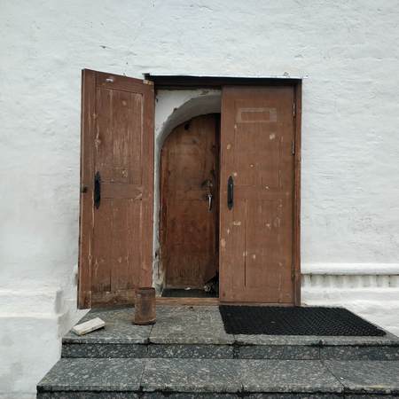An open wooden door on a white house. Element of the old church.