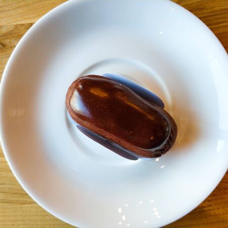 Mini eclair lies on a white saucer. Sweetness.