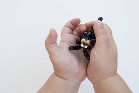 toy glass black cat in the hands of a young child on a white background. a small child of three years old is holding a black toy cat with yellow eyes in her handsの写真素材