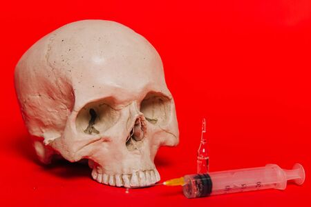 Human skull on a red background with an ampule and a syringe with a vaccine. The concept of death from the virus, death after vaccineの写真素材