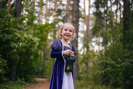 A little girl with white hair in a purple medieval dress stands with a lamp.の写真素材