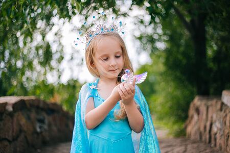 A little girl with white hair in a blue dress and with a crown on her head stands on the bridge.の写真素材