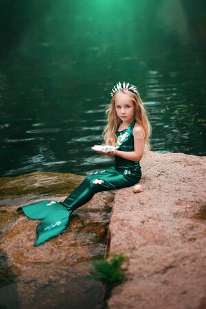A little girl with white hair with a mermaid tail and shells is sitting on the shore.の写真素材