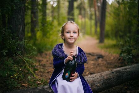 A little girl with white hair in a purple medieval dress sits on a tree with a lamp.の写真素材