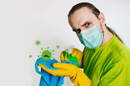 A guy in a green T-shirt and a medical mask holds in his hands a bulletizer with an antiseptic on a white background. A man kills a coronavirus.の写真素材
