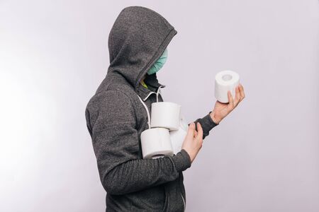 A guy in a gray sweatshirt and with rolls of toilet paper is standing on a white background. The excitement during quarantine for coronavirus.の写真素材