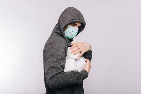 A guy in a gray sweatshirt and with rolls of toilet paper is standing on a white background. The excitement during quarantine for coronavirus.の写真素材