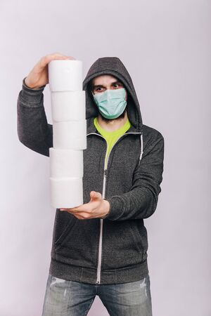 A guy in a gray sweatshirt and with rolls of toilet paper is standing on a white background. The excitement during quarantine for coronavirus.の写真素材