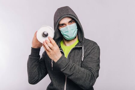A guy in a gray sweatshirt and with rolls of toilet paper is standing on a white background. The excitement during quarantine for coronavirus.の写真素材
