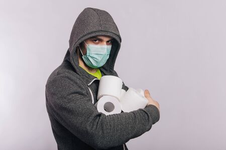 A guy in a gray sweatshirt and with rolls of toilet paper is standing on a white background. The excitement during quarantine for coronavirus.の写真素材