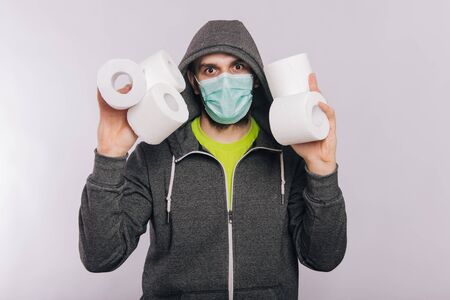 A guy in a gray sweatshirt and with rolls of toilet paper is standing on a white background. The excitement during quarantine for coronavirus.の写真素材