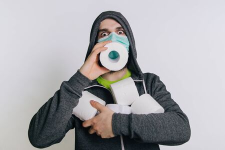 A guy in a gray sweatshirt and with rolls of toilet paper is standing on a white background. The excitement during quarantine for coronavirus.の写真素材