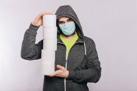 A guy in a gray sweatshirt and with rolls of toilet paper is standing on a white background. The excitement during quarantine for coronavirus.の写真素材
